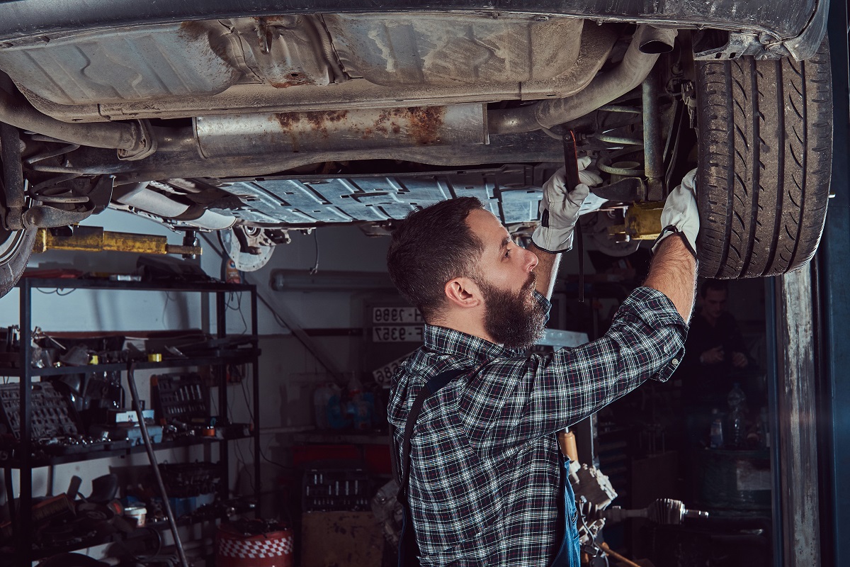 Two bearded brutal mechanics repair a car on a lift in the garage.