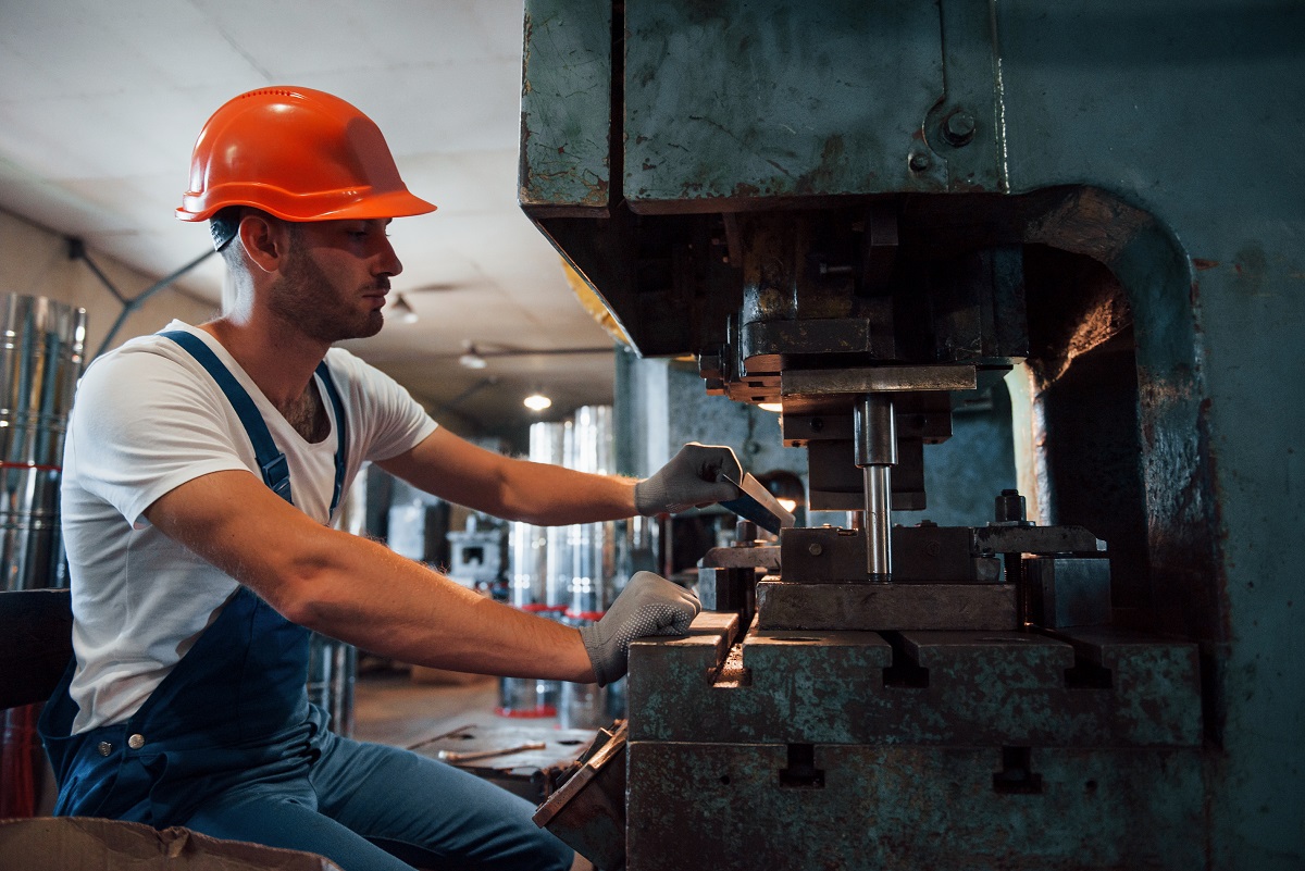 Puts sheet of metal in machine. Man in uniform works on the production. Industrial modern technology