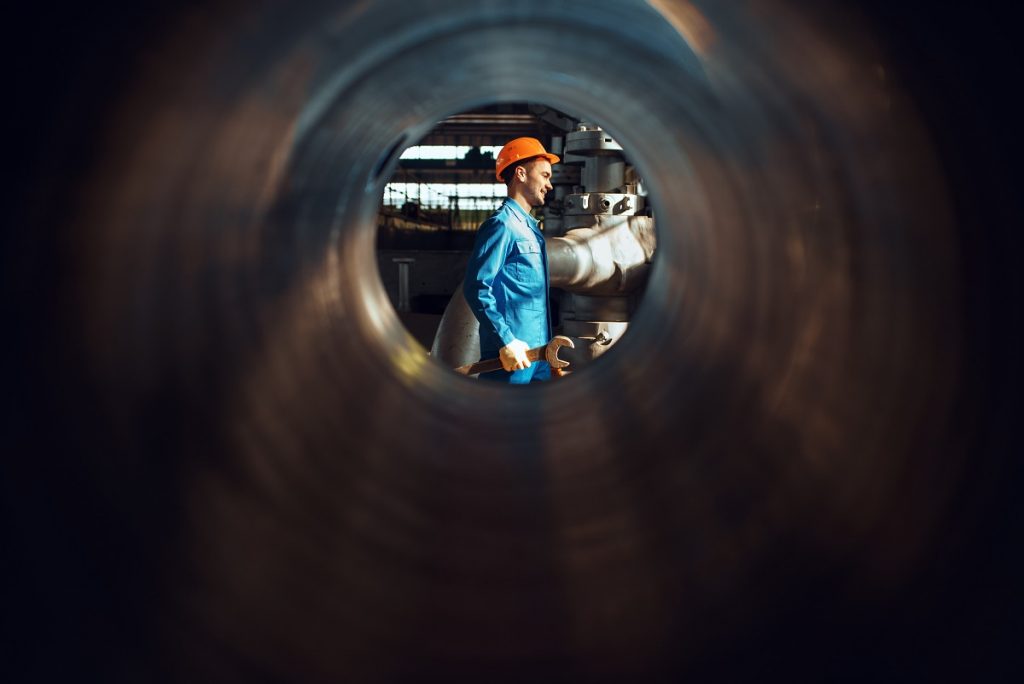 Worker with wrench on factory, view through tube