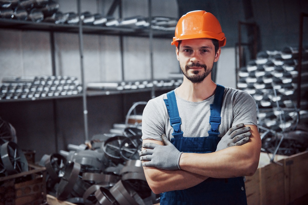 Portrait of a young worker in a hard hat at a large metalworking plant. Shiftman on the warehouse of finished products