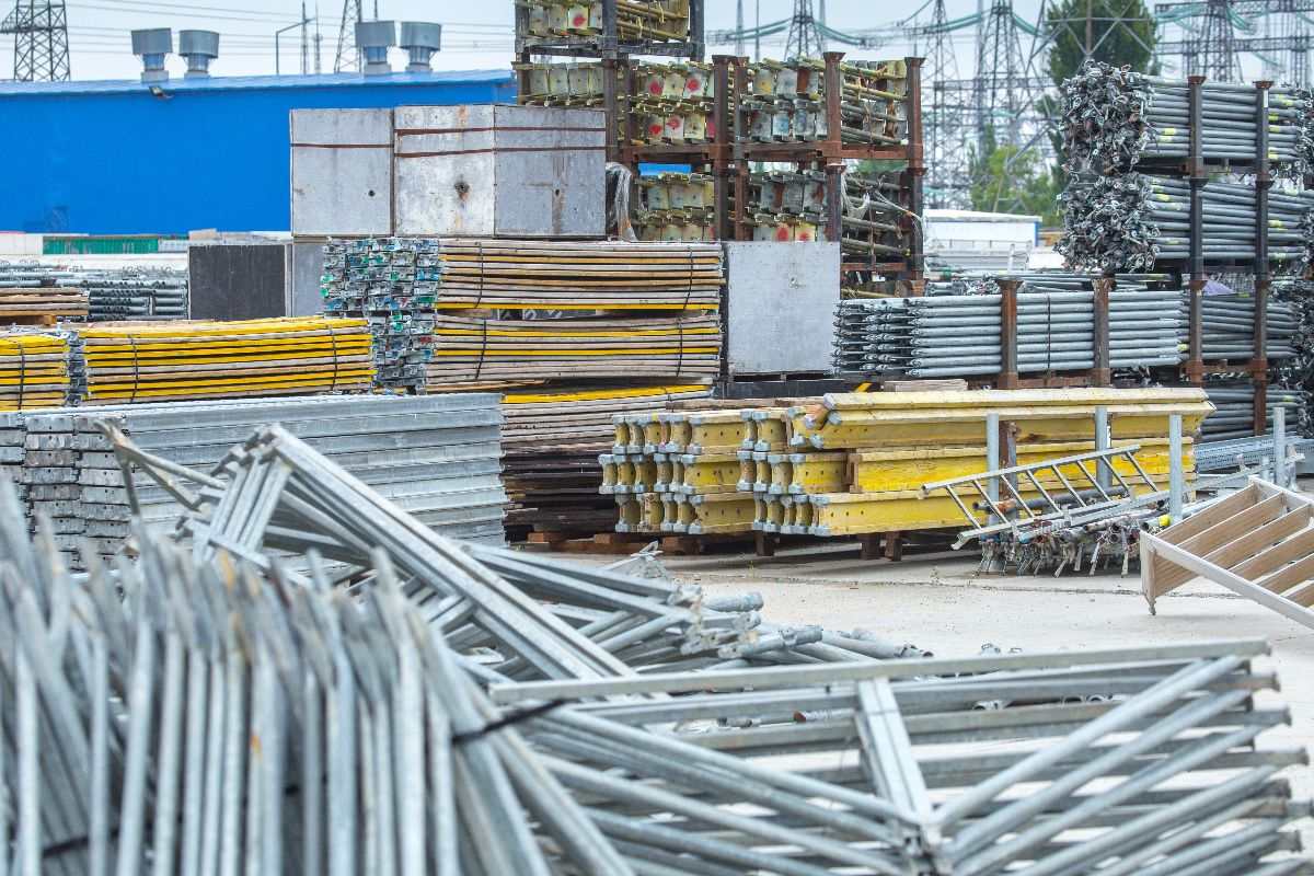 Steel components stacked outdoors with site materials and scaffolding equipment