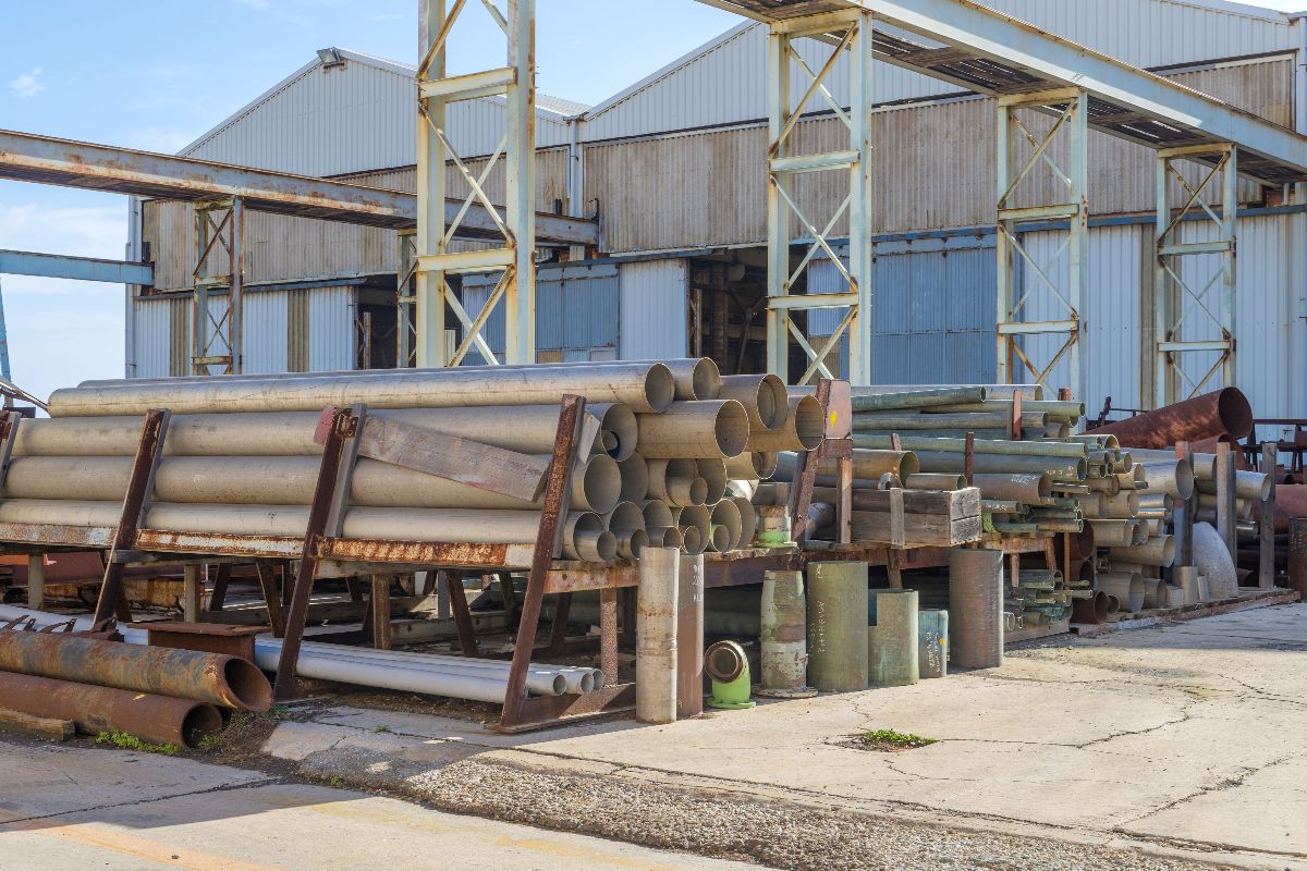 Steel pipes and construction materials stored outdoors near an industrial facility