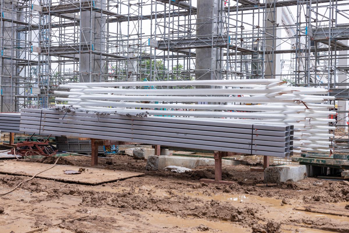 Stainless steel pipes and metal sections stored at a construction site with scaffolding