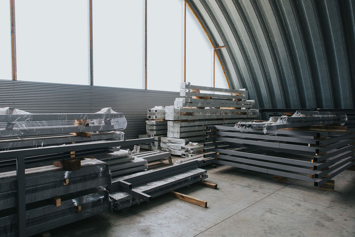 Stacks of wrapped steel beams and fabricated metal components stored inside an industrial warehouse