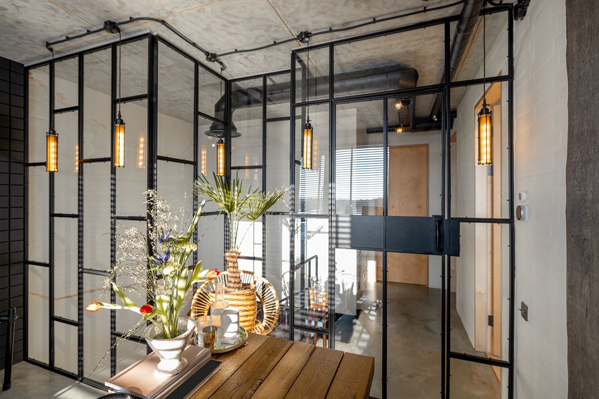 Modern interior with black steel-framed glass partitions, warm pendant lights, and a wooden table