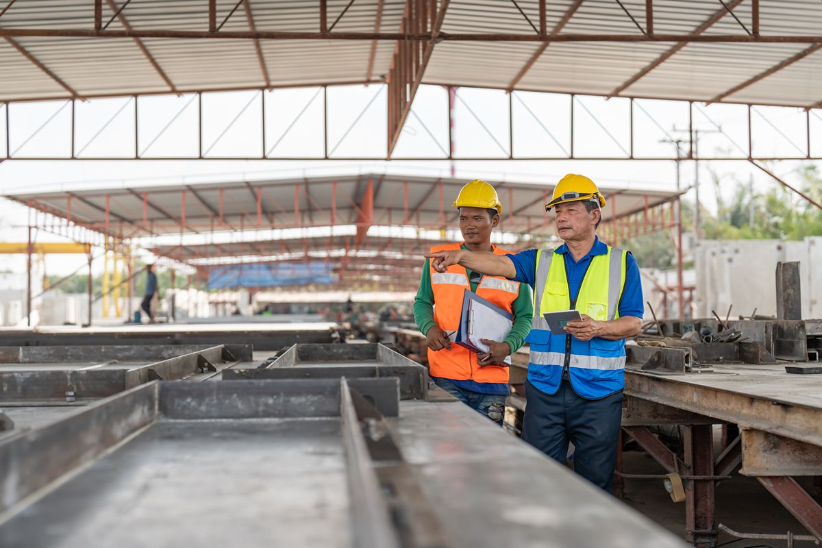 Two workers inspecting fabricated steel components inside a covered industrial facility